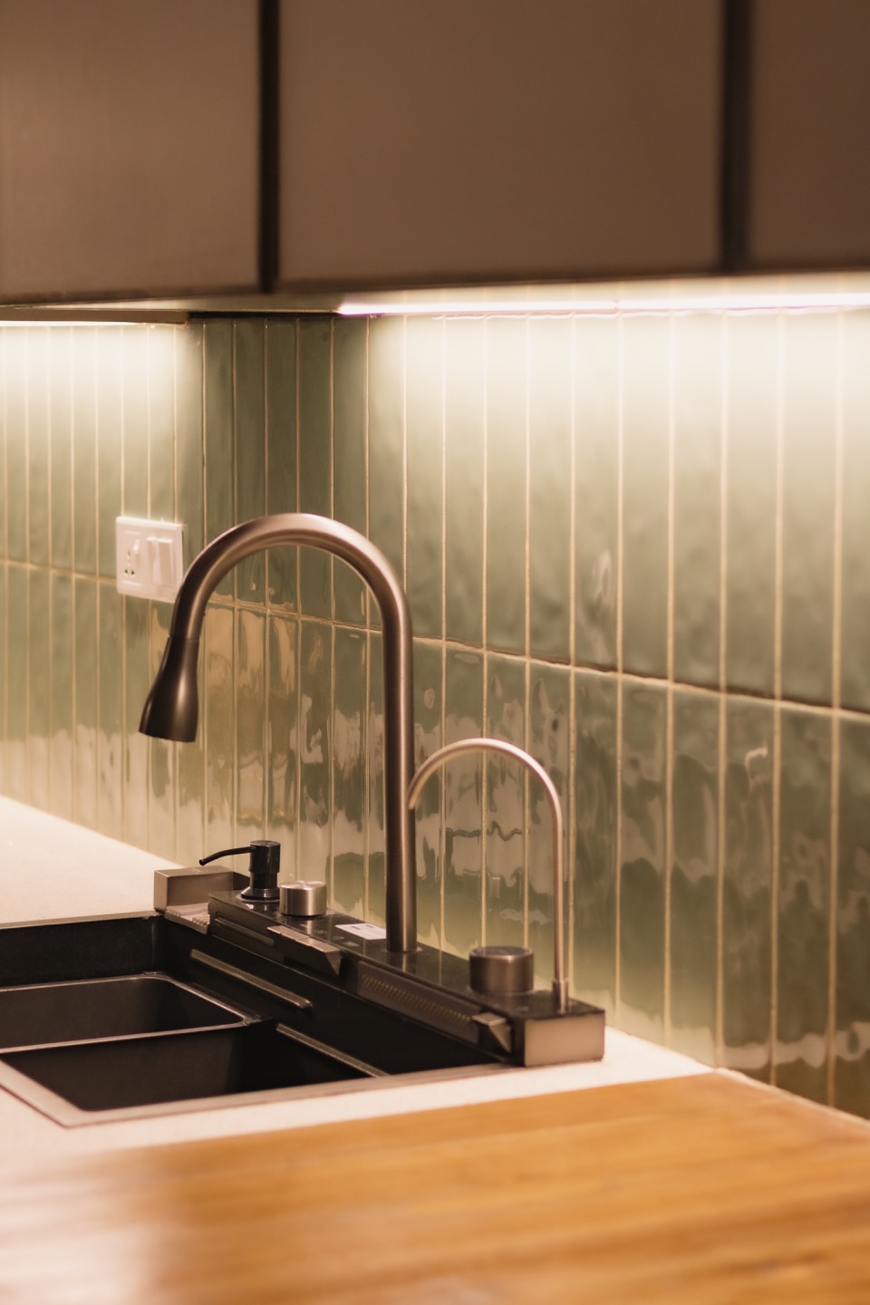 Kitchen sink framed by green tile and warm timber
