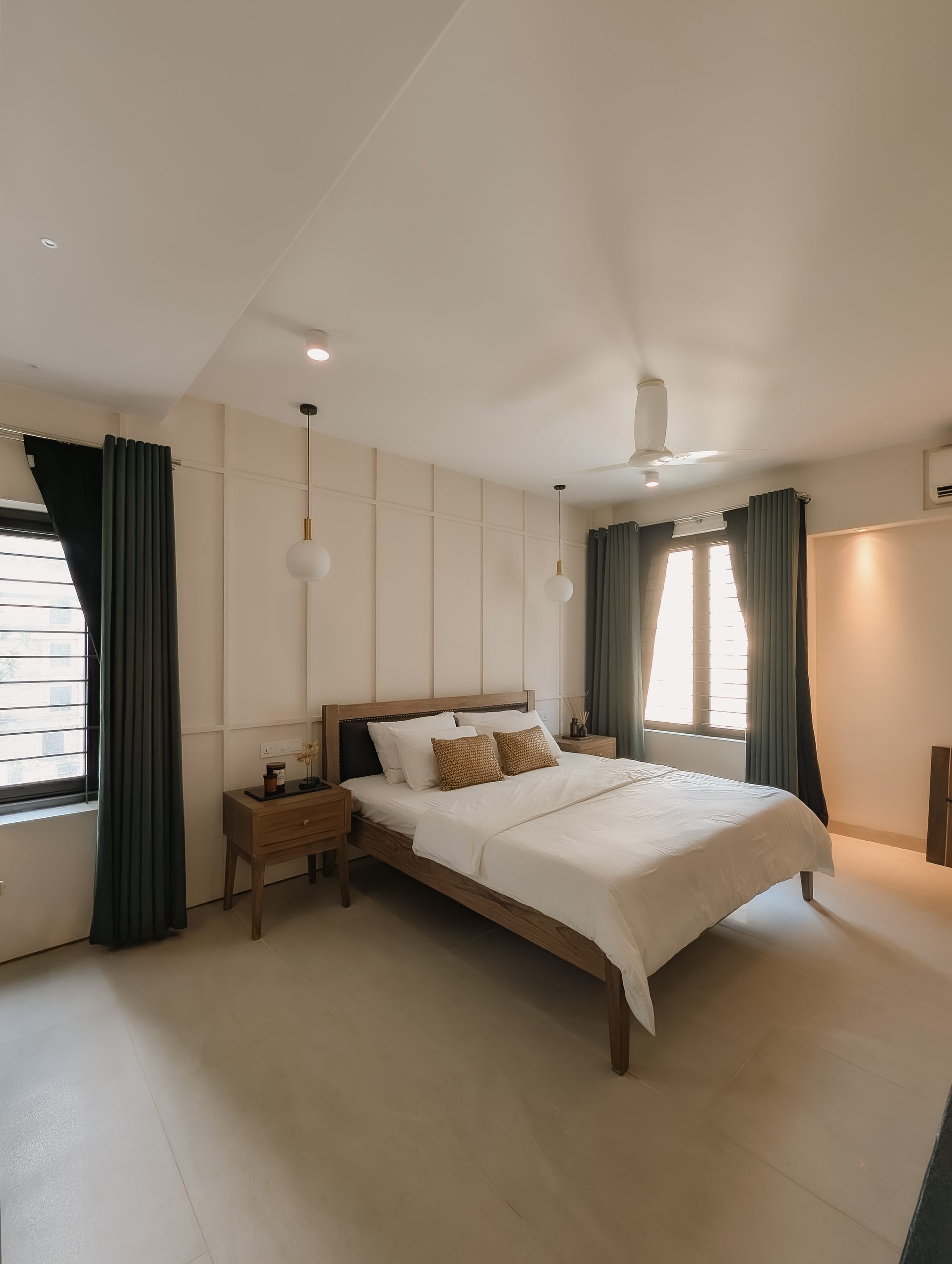 Primary bedroom viewed across its teak bed toward deep green curtains and windows