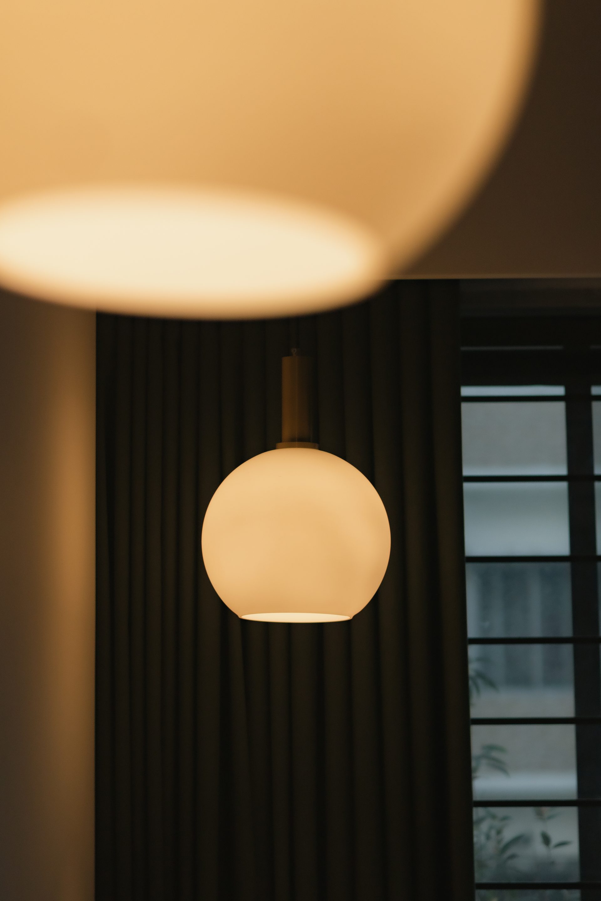 Close view of a glowing globe pendant against the bedroom curtain