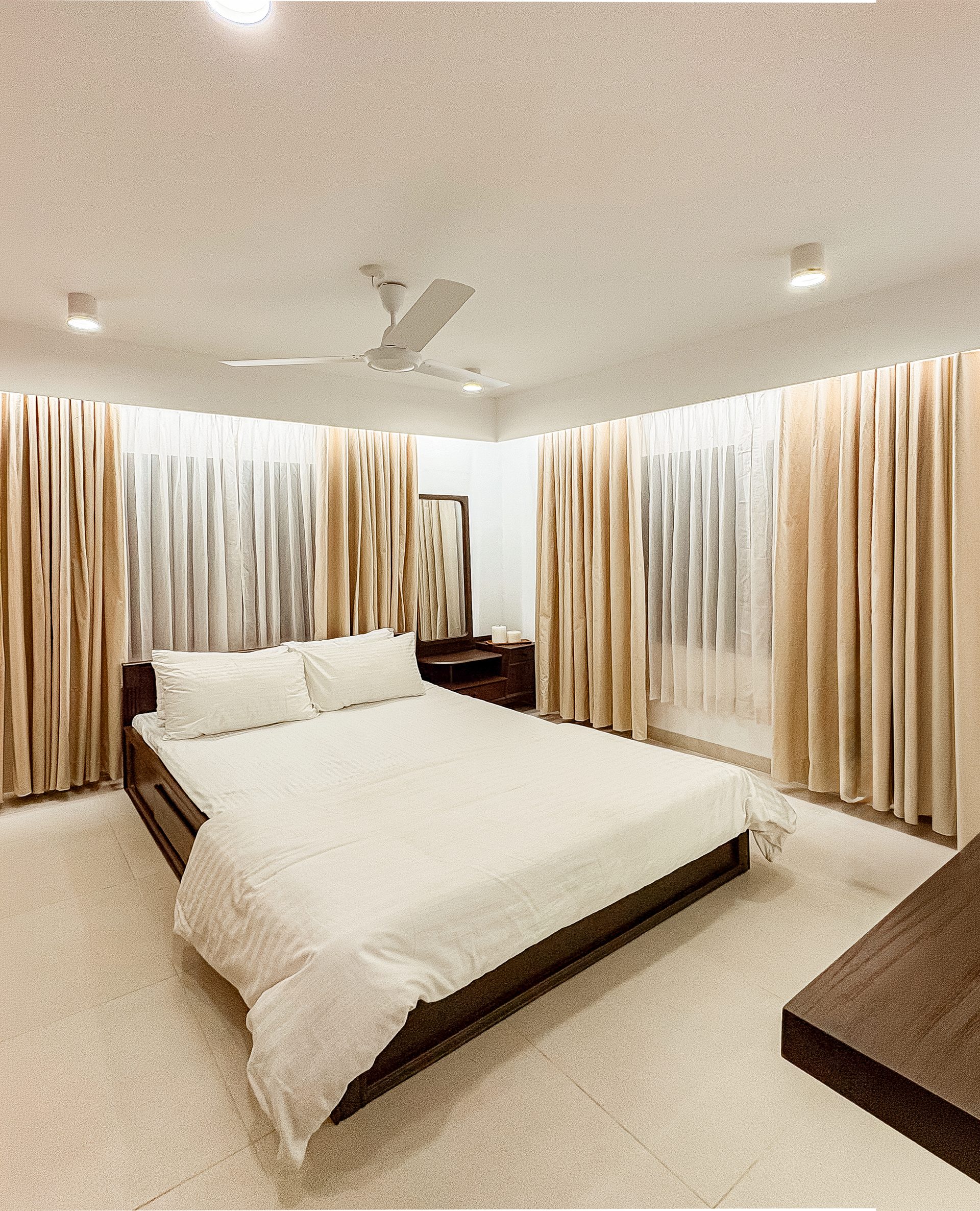 Cream primary bedroom with a dark timber bed and layered curtains