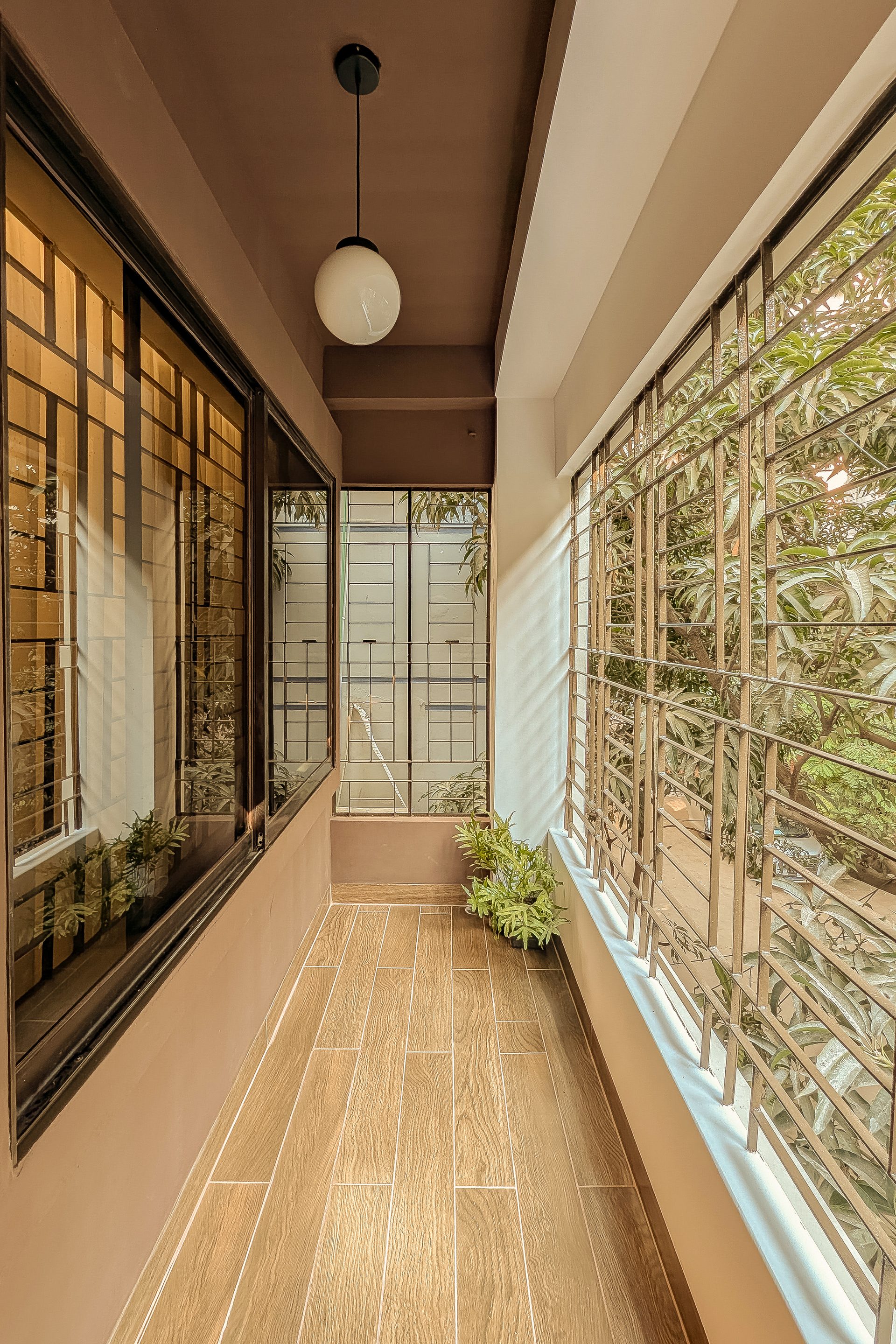 Narrow planted guest-room balcony with warm timber floor tiles and leafy views