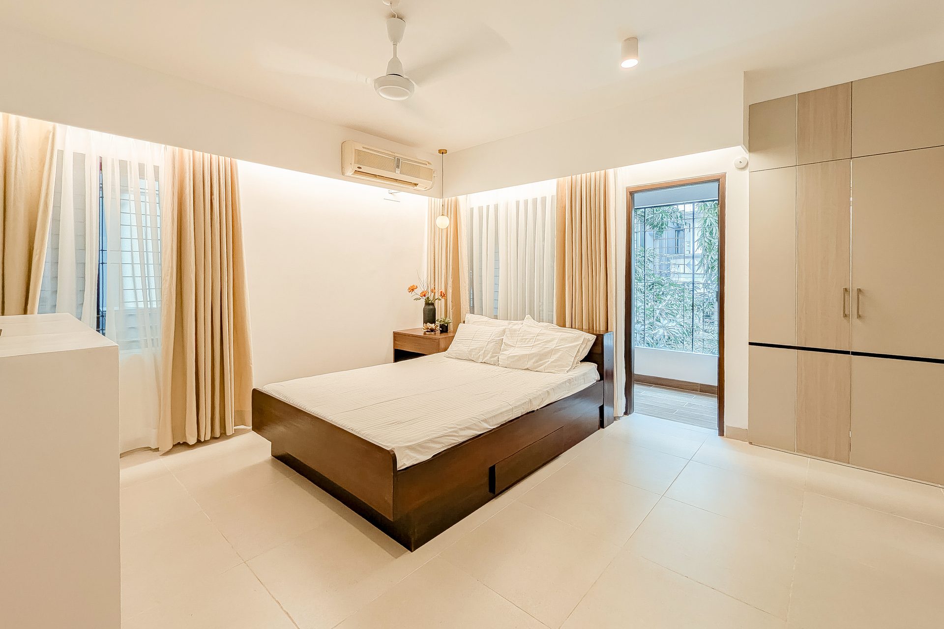 Light guest bedroom with a dark timber bed and full-height curtains