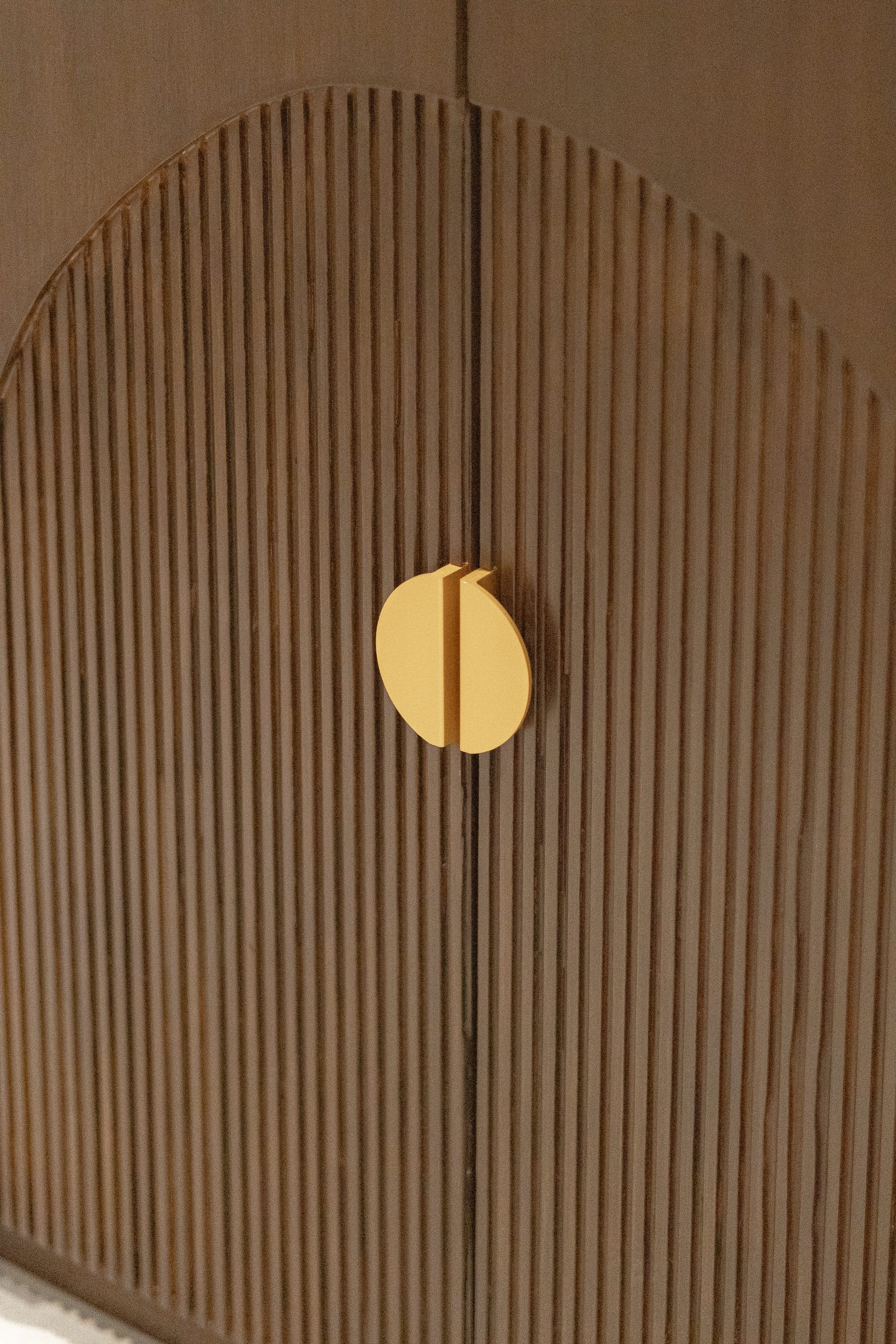 Circular brass handle set into vertically fluted dark timber